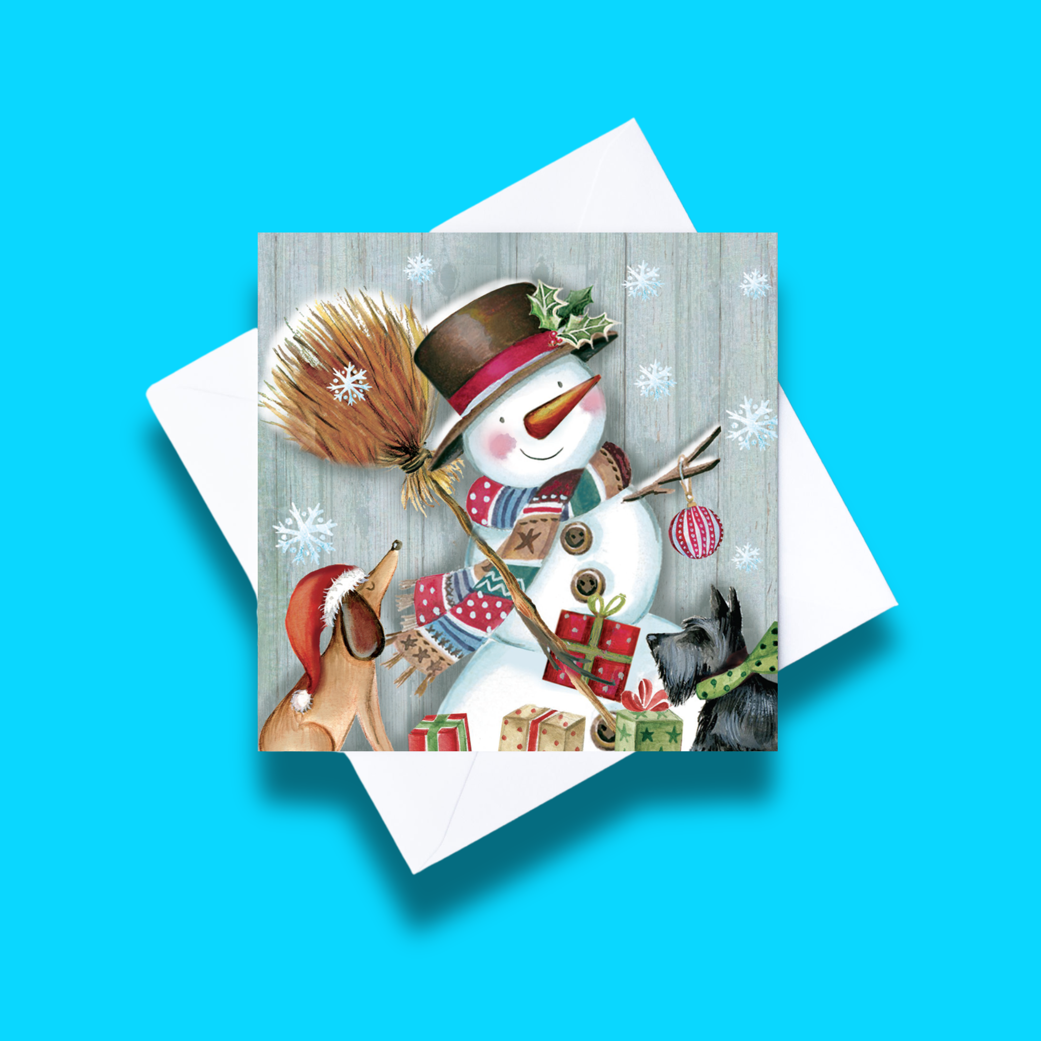 Snowman and Friends Christmas card with white envelope on a blue background. Card design features a decorated snowman and two dogs with a broom and presents.